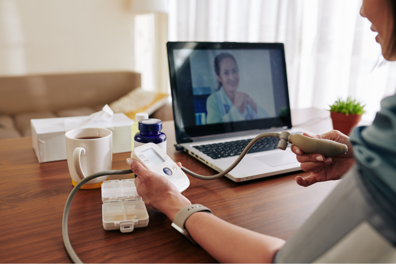 Woman measuring her blood pressure at home while consulting a healthcare professional on screen, highlighting the cost of remote patient monitoring.