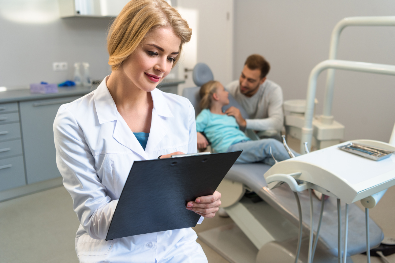 Female dentist reviewing billing records while child and father wait, representing outsource dental billing and dental insurance outsourcing.